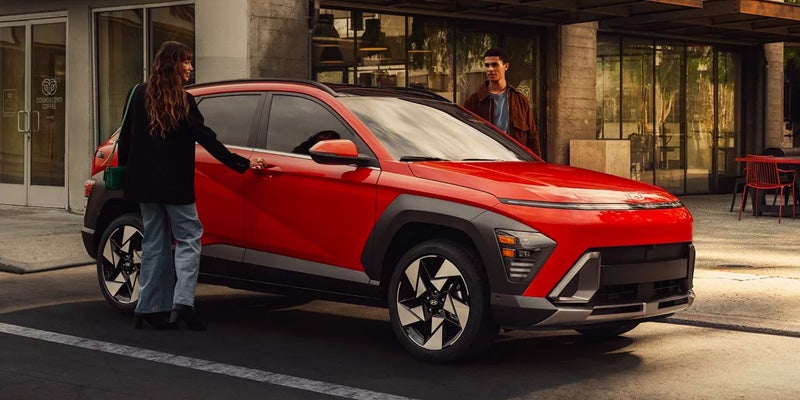 Red Hyundai Kona parked roadside with couple opening doors
